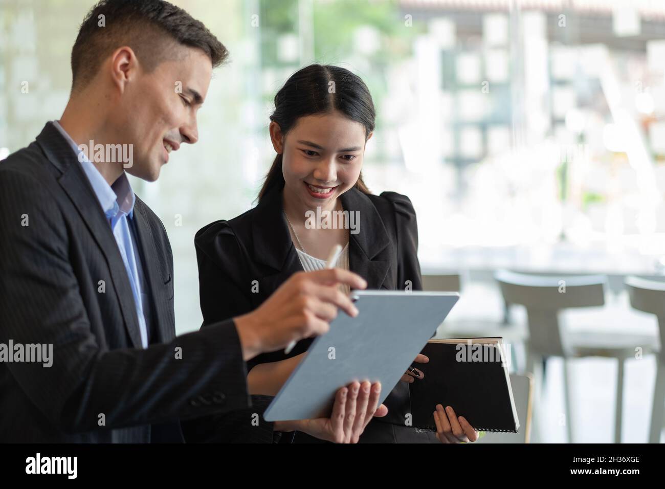Fokussierte Mitarbeiter verschiedener ethnischer Herkunft führen Brainstorming auf einem digitalen Tablet durch, asiatische und kaukasische Kollegen tauschen Ideen am Schreibtisch aus Stockfoto