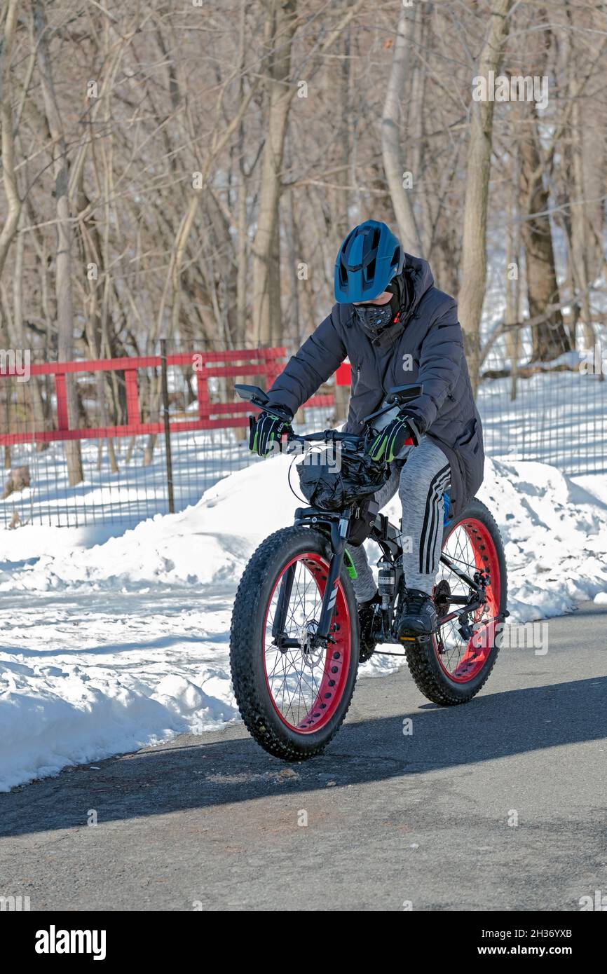 Ein Mann mit Helm und ausgeklügelter Maske radeln an einem kalten Wintertag um den See im Kissena Park. Stockfoto