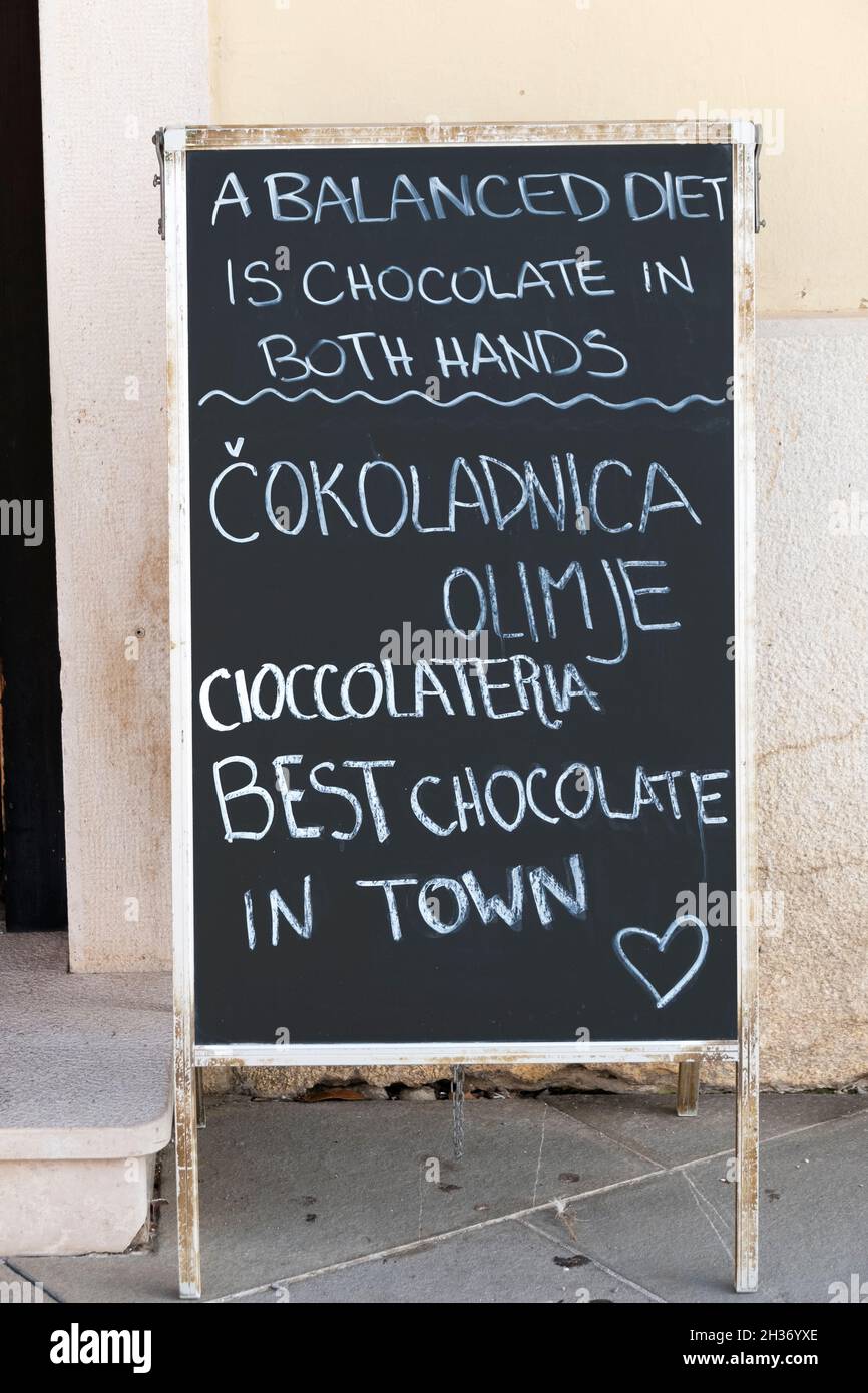 Ein lustiges Schild vor einem Schokoladengeschäft in Piran, Slowenien, das besagt, dass eine ausgewogene Ernährung Schokolade in beiden Händen ist. Stockfoto