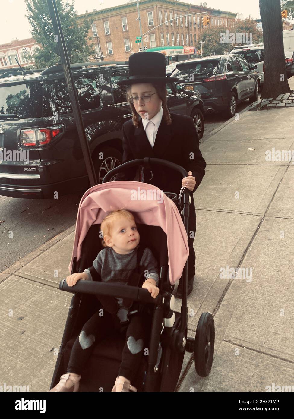 Der orthodoxe jüdische Junge schiebt einen Geschwister in einen Kinderwagen im Stadtteil Borough Park in Brooklyn, New York. Stockfoto