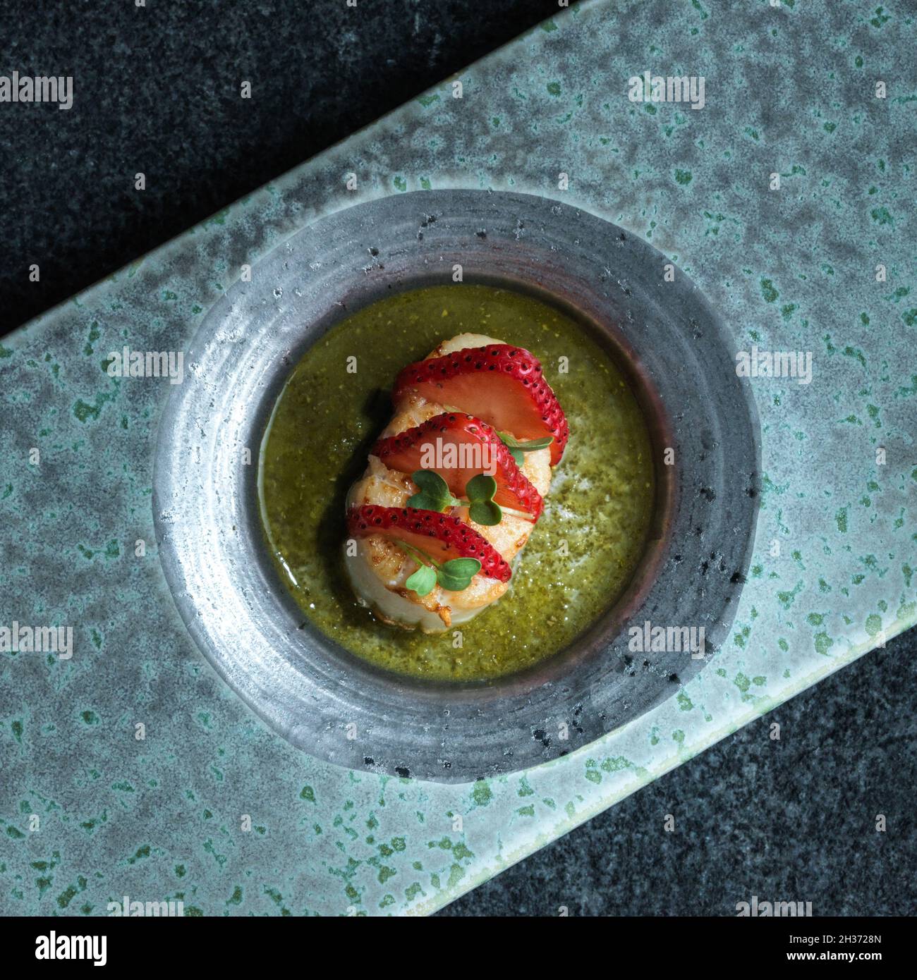 Jakobsmuschel in Scheiben geschnitten mit Erdbeerscheiben auf Zitronensalsa verde Stockfoto