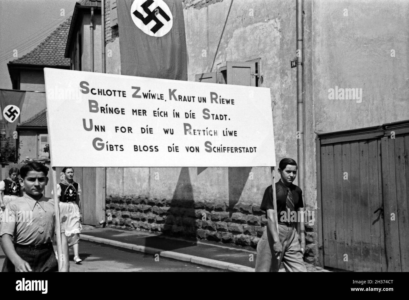 Jugendliche gürteltaschen einTransparent mit einem Rettich Werbespruch beim Festzug zum Rettichfest in Schifferstadt, Deutschland, 1930er Jahre. Jugendliche mit einem Banner, auf dem ein Werbeslogan für radieschen am Pageant der jährlichen Rettich Messe in Schifferstadt, Deutschland 1930. Stockfoto