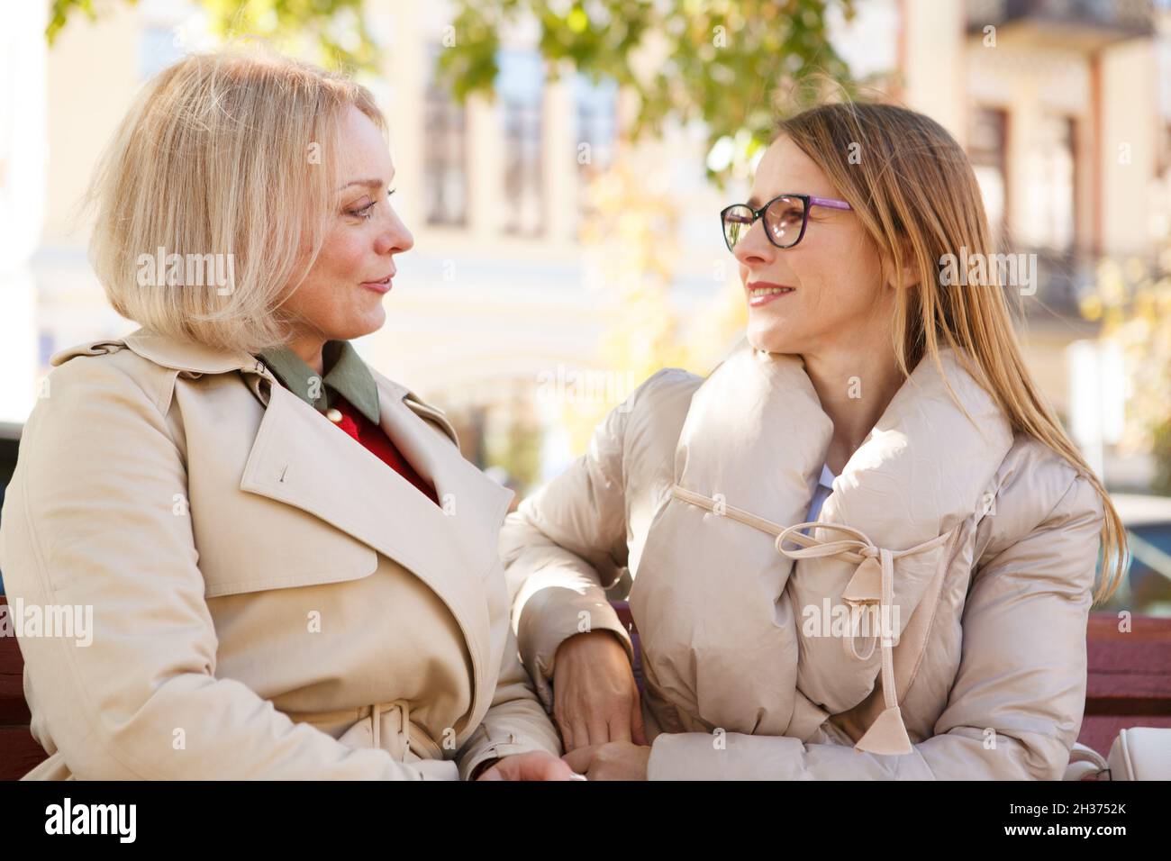 Zwei Frauen mittleren Alters, die sich am warmen Herbsttag im Park ausruhen und sich freudig unterhalten Stockfoto