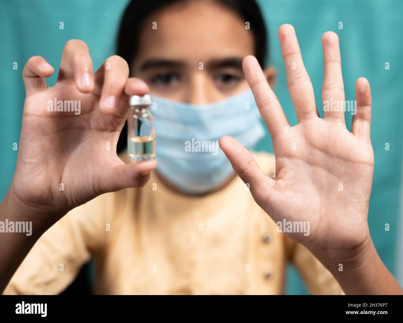 Selektiver Fokus auf der Hand, Kind mit medizinischer Gesichtsmaske, das Nein zur Covid-19- oder Coronavirus-Impfung sagt, indem es Handgesten und Impfstoff zeigt Stockfoto