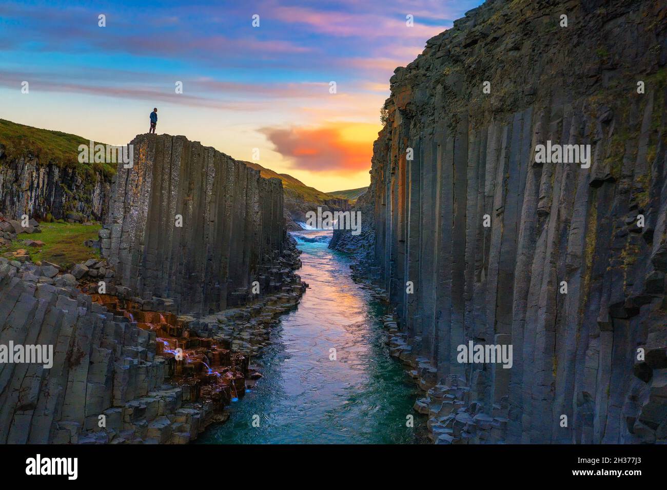 Wanderer, der bei Sonnenuntergang auf dem Gipfel des Studlagil Canyon in Island steht Stockfoto