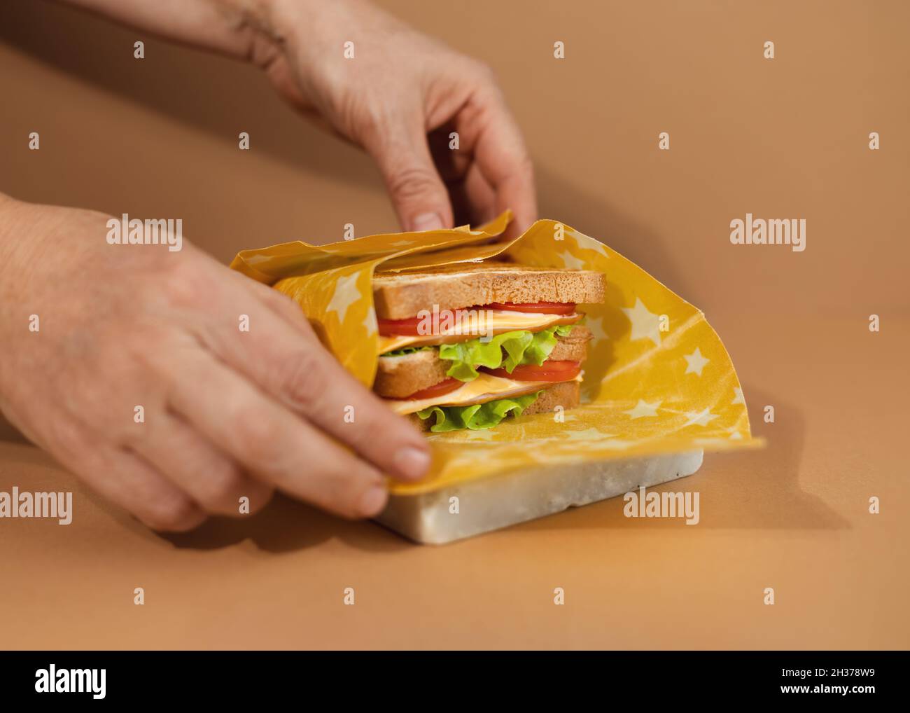 Ein traditionelles Sandwich aus getoasteten Brotscheiben, Käse, Schinken und frischem Salat, eingewickelt in wiederverwendbares Bienenwachspapier aus biologischem Anbau. Wir Feiern National Sandwi Stockfoto