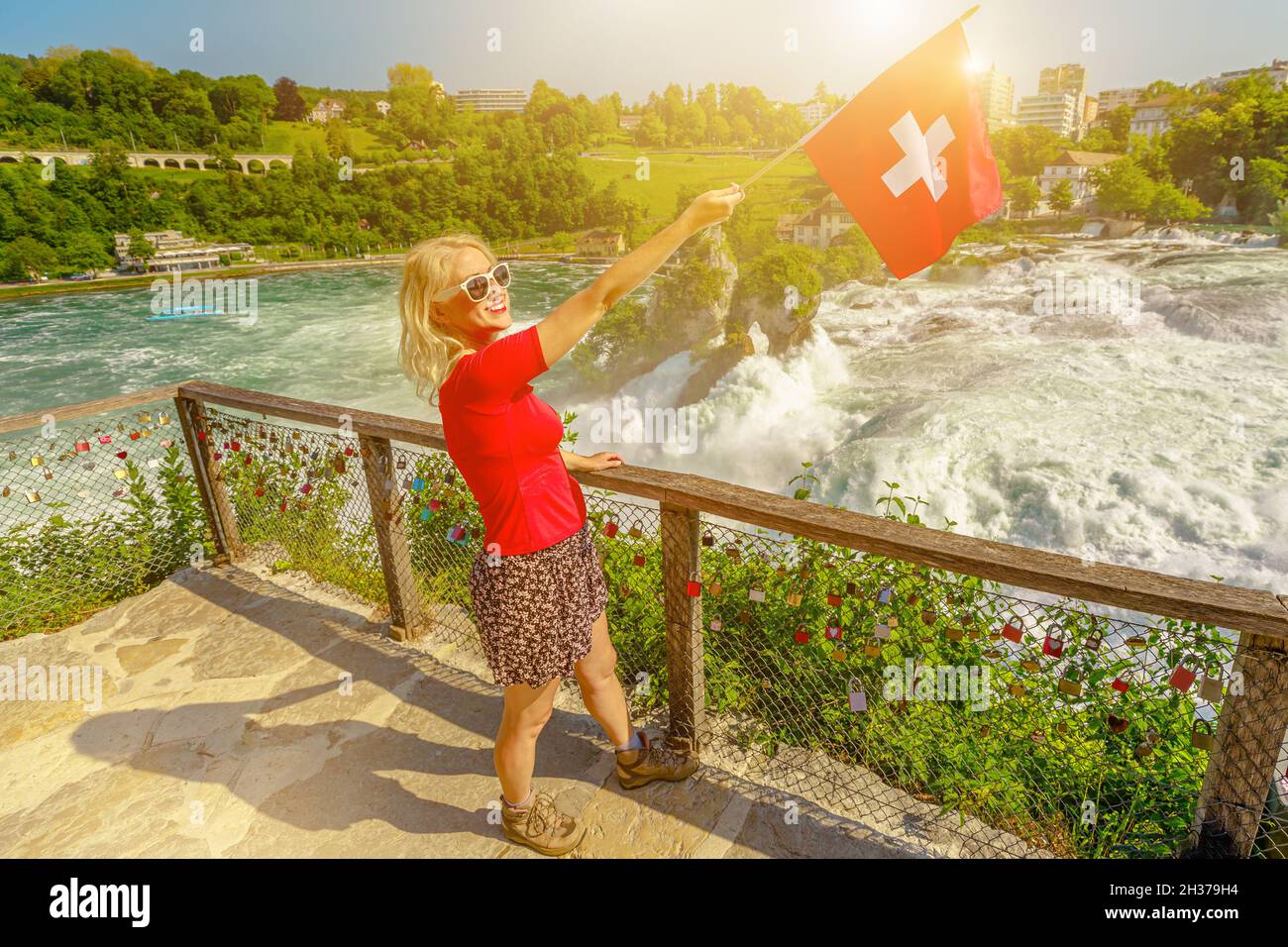 Nahaufnahme einer Schweizer Frau mit schweizer Flagge bei Sonnenuntergang. Luftaufnahme des Schweizer Wasserfalls Rheinfall in der Schweiz. Der mächtigste und größte Wasserfall in Stockfoto