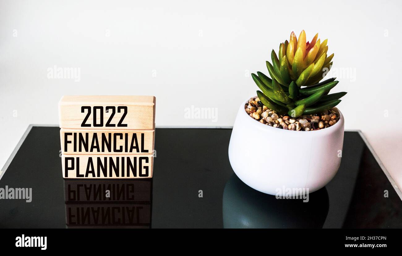 Holzblöcke mit dem Text 2022 FINANZPLANUNG stehen auf einem schwarz-weißen Tisch mit einem Kaktus Stockfoto