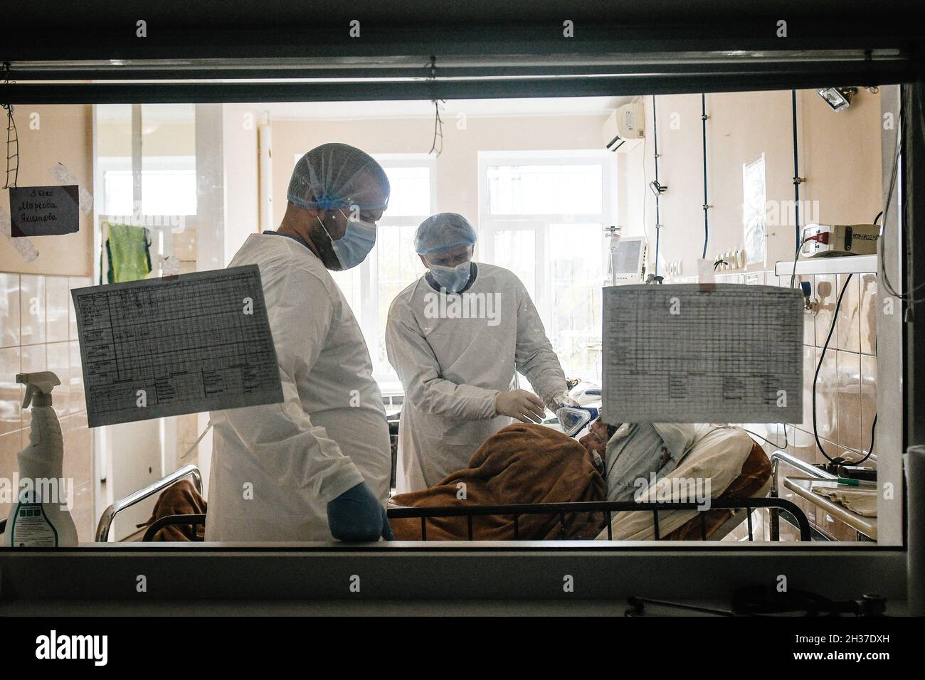 ZAPORIZHZHIA, UKRAINE - 25. OKTOBER 2021 - Ärzte betreuen einen Patienten, wie sie durch ein Fenster in der Intensivstation COVID-19 des regionalen Infektionskrankenhauses Zaporizhzhia, Saporizhzhia, im Südosten der Ukraine gesehen werden. Stockfoto