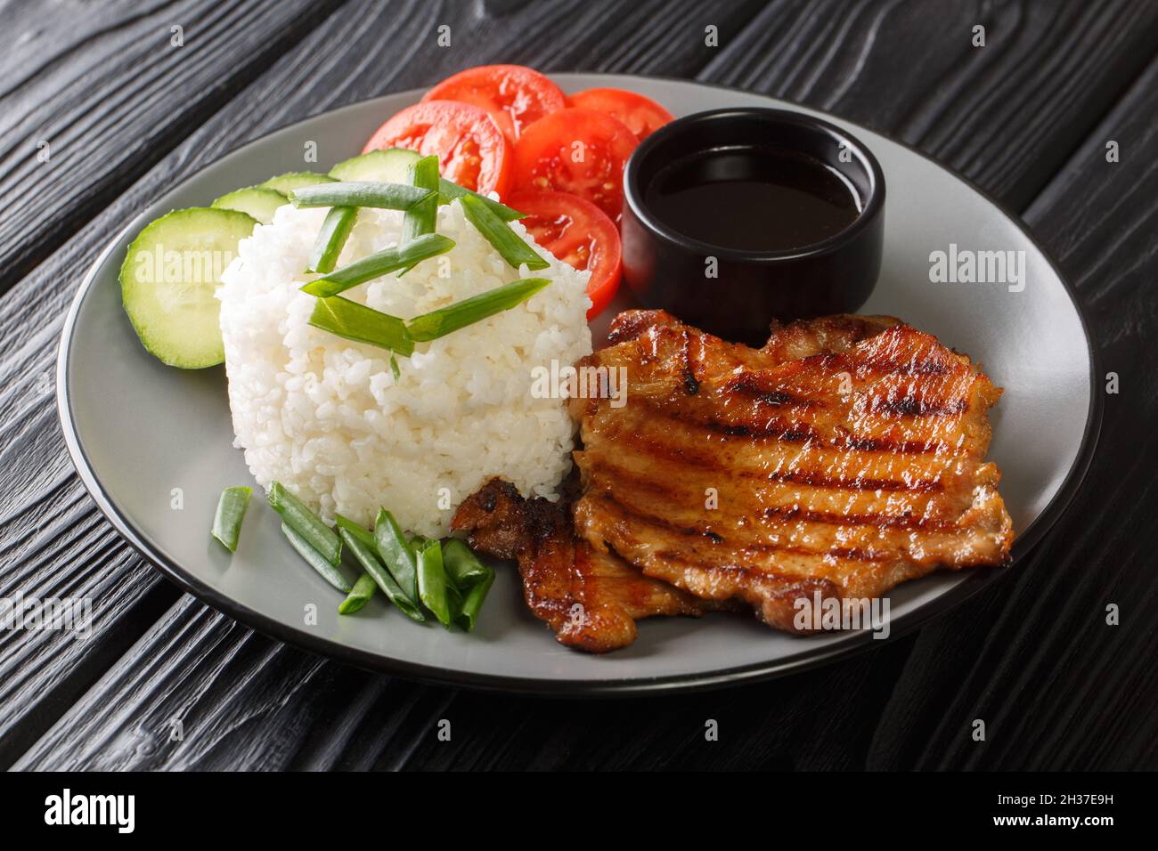Vietnamesisches Essen gebrochener Reis mit gegrilltem Schweinefleisch und frischem Gemüse aus der Nähe in einem Teller auf dem Tisch. Horizontal Stockfoto