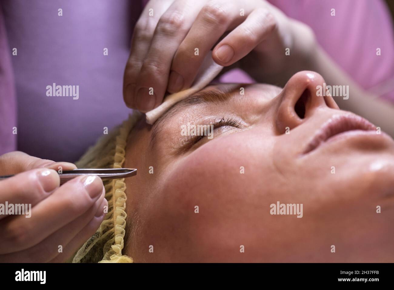 Makeup-Künstler pflückt Augenbrauen mit einer Pinzette einer Frau nach einem kosmetischen Eingriff. Stockfoto