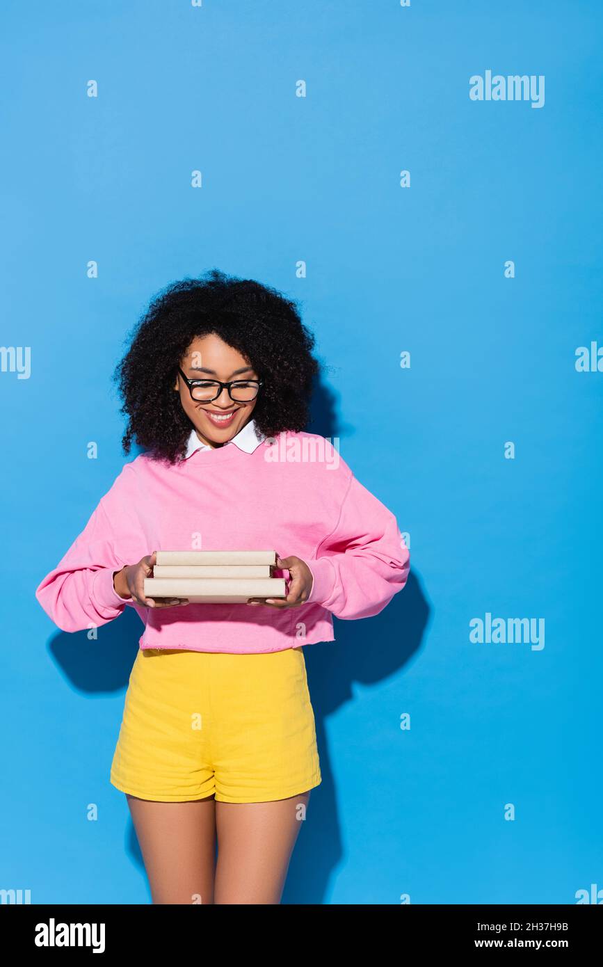 Glückliche afroamerikanische Frau in Brillen mit Büchern auf Blau Stockfoto