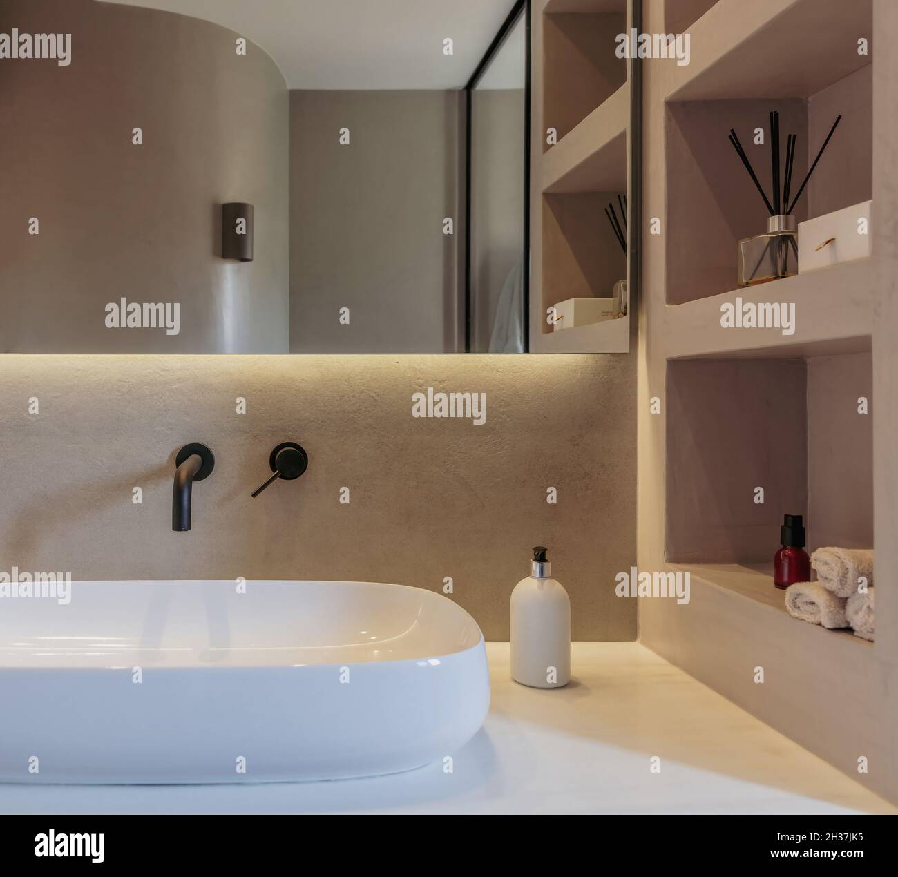 Die Einrichtung des Badezimmers ist minimalistisch. Rundes Waschbecken auf einer weißen Marmortheke, schwarze Wasserhähne an der grauen Wand, Spiegel und lineares LED-Licht. Moderne Accessoires a Stockfoto
