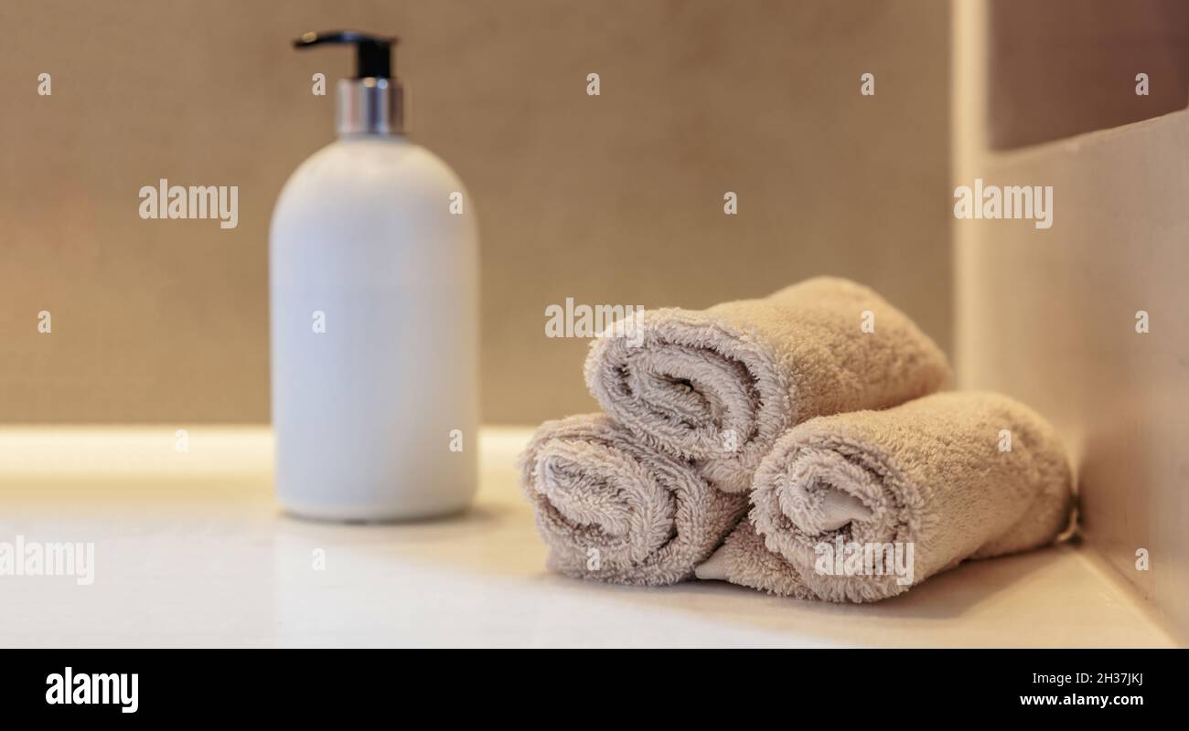 Inneneinrichtung des Badezimmers. Saubere Handtuchrollen, Seifenspender und weißes Waschbecken auf einem Tisch, Banner Stockfoto