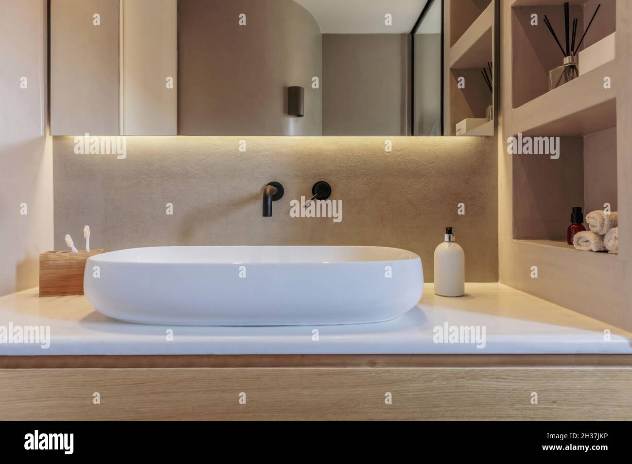 Waschbecken im Badezimmer auf einer weißen Marmortheke, schwarze Wasserhähne an der grauen Wand, Spiegel und lineares LED-Licht. Moderne Accessoires und Ausstattung, Interieur minimal Stockfoto