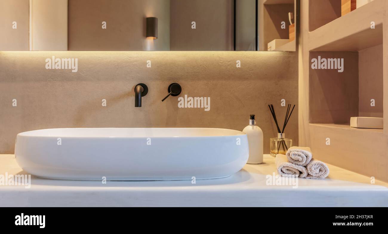 Die Einrichtung des Badezimmers ist minimalistisch. Rundes Waschbecken auf einer weißen Marmortheke, schwarze Wasserhähne an der grauen Wand, Spiegel und lineares LED-Licht. Moderne Accessoires a Stockfoto