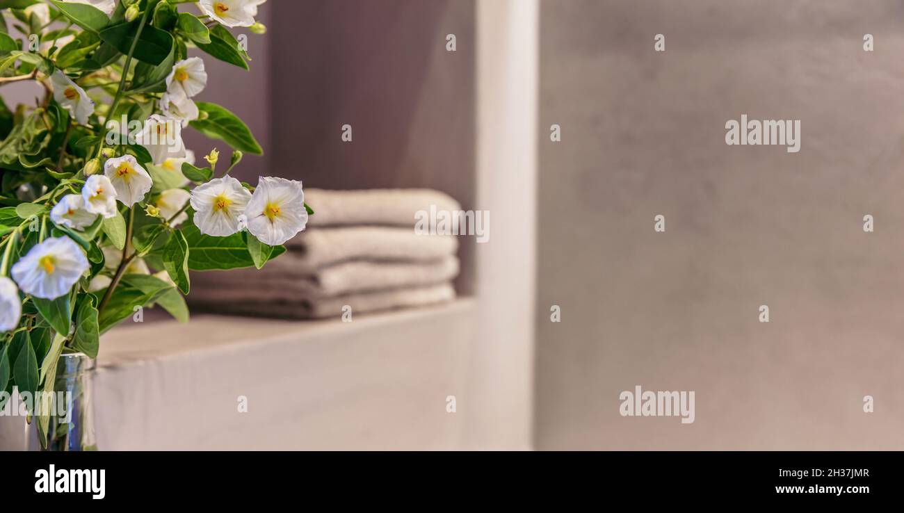 Badezimmer mit moderner Innenausstattung. Frische blühende Pflanze aus der Nähe, verschwommener Hintergrund, Handtücher auf einem Regal gestapelt. Leerer Raum, Spa Wellness-Raum verlockt Stockfoto