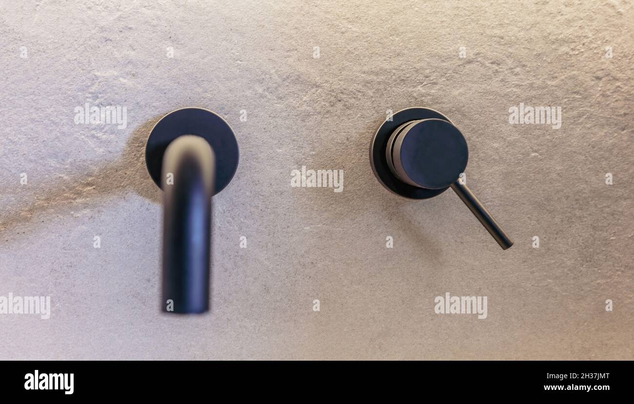 Moderne schwarze farbige runde Waschtisch-Armaturen, die an der grau gefliesten Wand montiert sind. Moderne Badezimmer Innenausstattung, Waschbecken Armaturen, minimalistisches Design, Vorderansicht Stockfoto