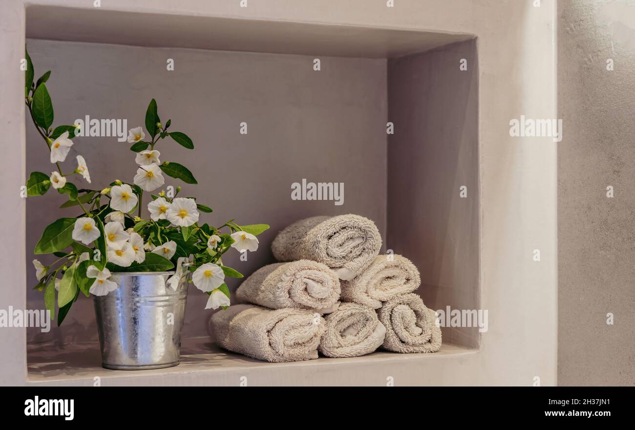 Handtücher im Bad gefaltet auf einem Wandregal gestapelt. Frische weiß blühende Topfpflanzen Dekoration. Moderne Inneneinrichtung. Stockfoto