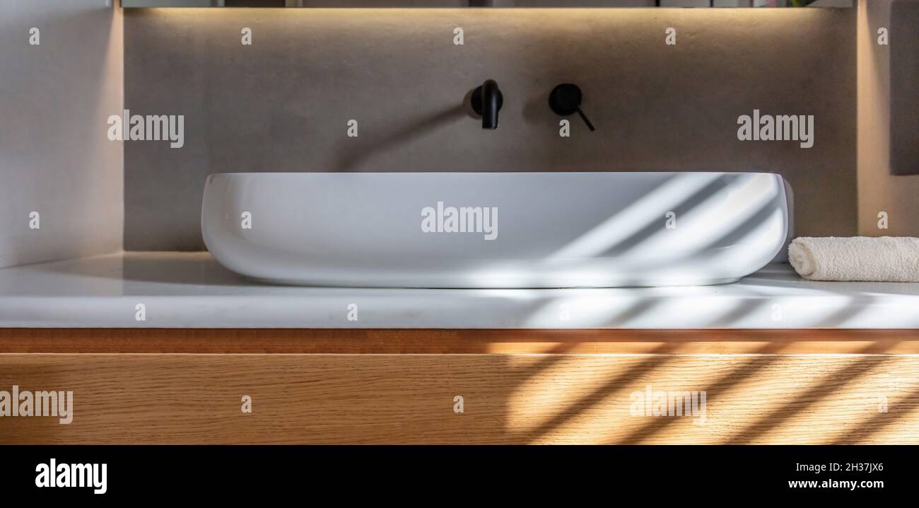 Badezimmer modernes Waschbecken auf weißem Marmortisch, schwarze Wasserhähne an grauer Wand, lineares LED-Licht. Rundes Waschbecken und Armaturen Detail, innen minimal de Stockfoto