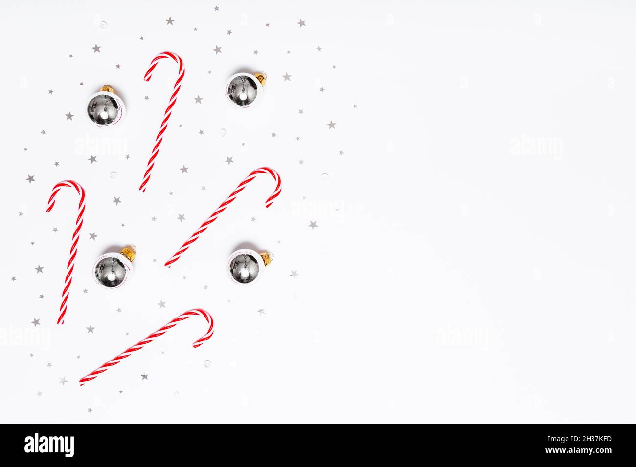 Weihnachten flach Lay Zusammensetzung. Weihnachtsbonbons, silberne Kugeln, glitzernde Konfetti-Sterne auf weißem Hintergrund. Flaches Design, Draufsicht, Kopierbereich Stockfoto