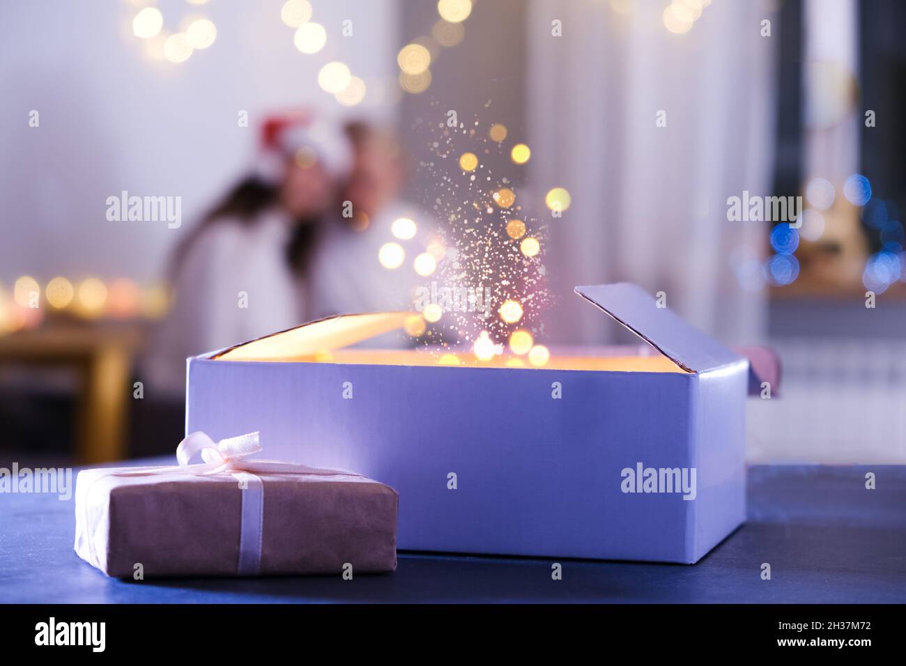 Person öffnet Geschenk, Wunder und Wünsche werden am Heiligabend wahr. Nahaufnahme der Hände mit Neujahrsgeschenk zu Hause in der Nacht. Magischer Hintergrund mit Staub Stockfoto