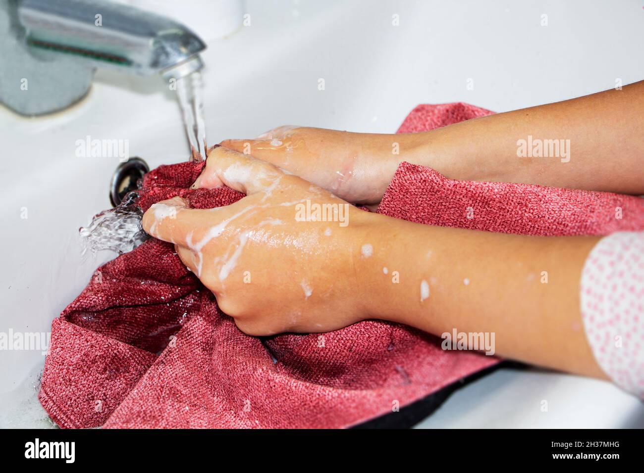 Händewaschen von farbigen Dingen. Frauenhände waschen und wringen farbige Dinge in Seifenwasser aus. Stockfoto