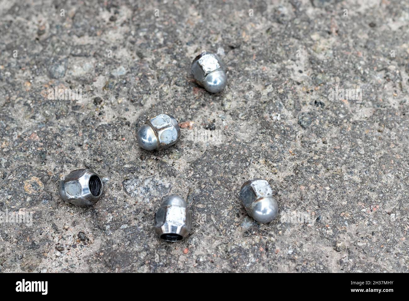 Fünf Radmuttern, mit denen das Rad an der Nabe befestigt ist, liegen beim Austauschen auf dem Bürgersteig in der Nähe der Autoreifenwerkstatt. Selektiver Fokus. Nahaufnahme Stockfoto