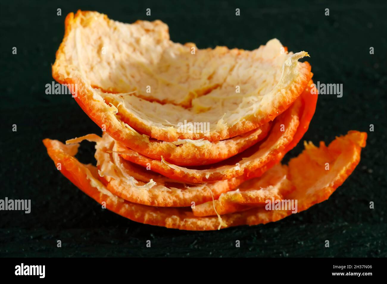 Orangenschale von Mandarinenfrüchten auf dunkelgrünem Hintergrund dargestellt. Stockfoto