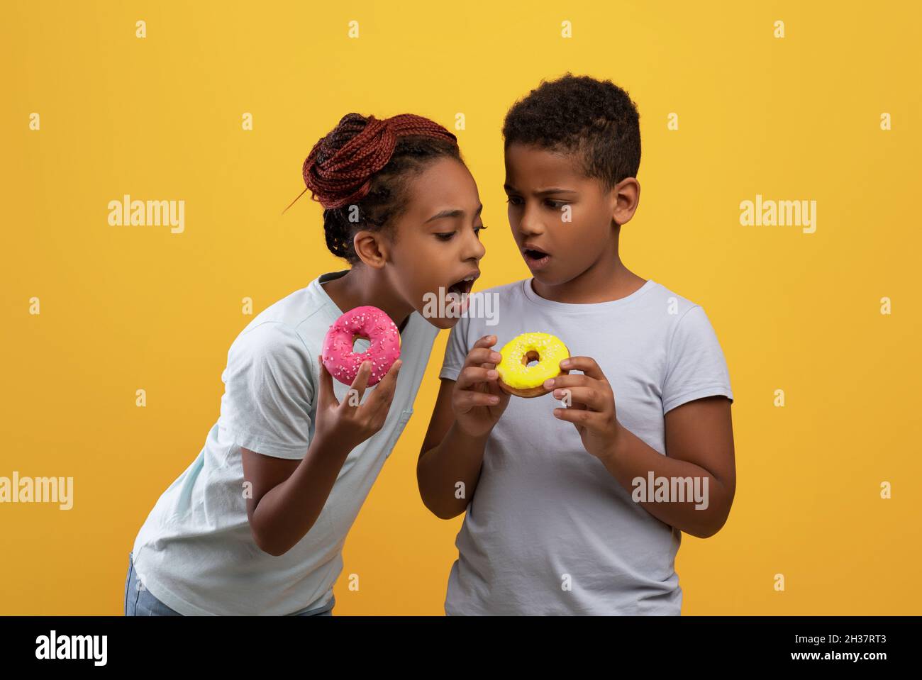 Süßes schwarzes Mädchen, das ihre Brüder auf Donut beißt Stockfoto