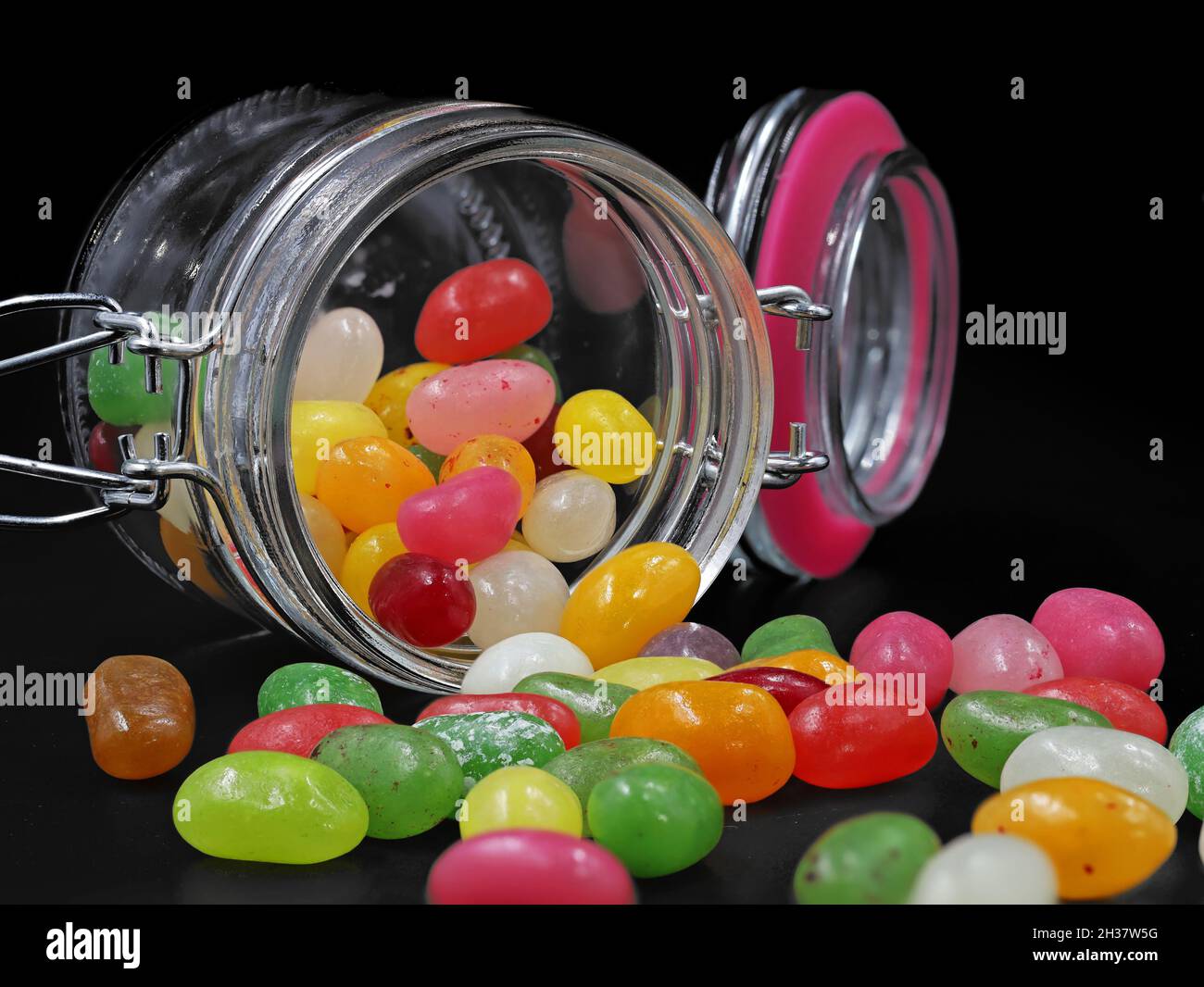 Glas mit bunten Jelly Beans verschüttet auf schwarzem Hintergrund Stockfoto