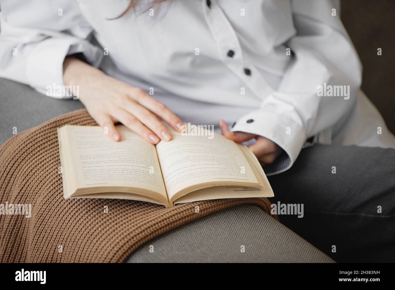 Nahaufnahme einer Frau, die Buch auf dem Sofa hält und liest. Stockfoto