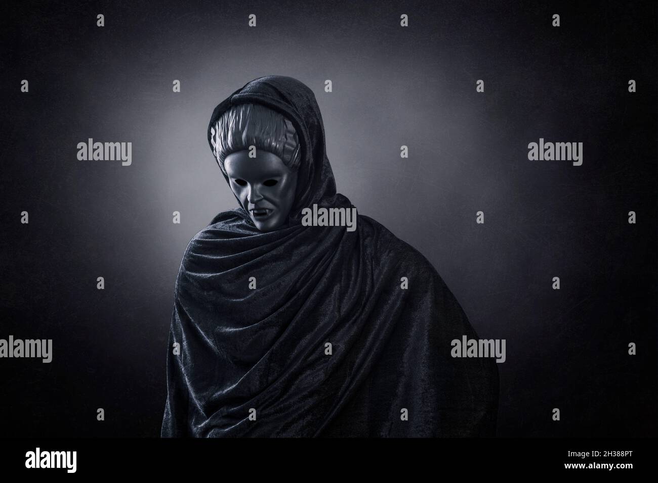 Frauengeist im Kapuzenmantel über dunklem nebligen Hintergrund Stockfoto
