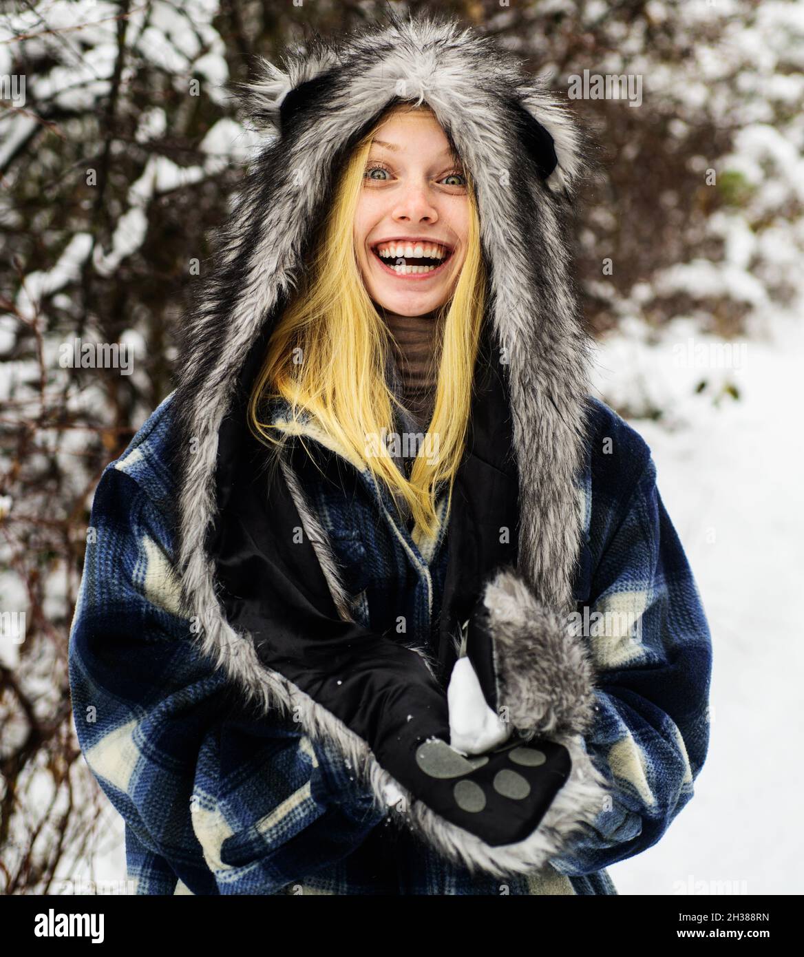 Nette Frau, die mit Schnee spielt. Mädchen in Fäustlingen halten Schneeball. Winterzeit. Lächelnde Frau in warmer Kleidung. Wintersaison. Stockfoto