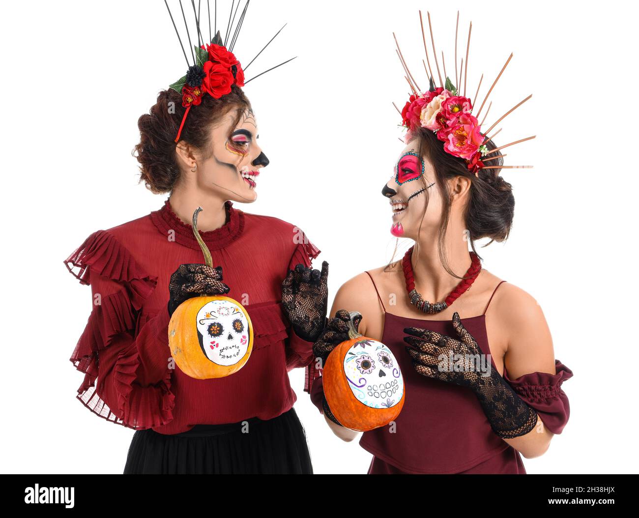 Stylische Frauen mit bemaltem Schädel auf Gesichtern und Kürbissen vor weißem Hintergrund. Feier des mexikanischen Tages der Toten (El Dia de Muertos) Stockfoto