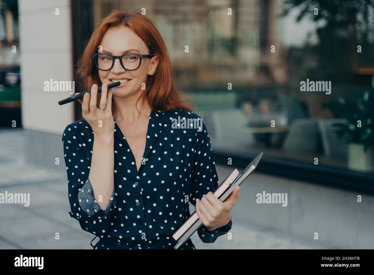 Rothaarige erfolgreiche Geschäftsfrau zeichnet Sprachnachricht auf und hält das Smartphone in der Nähe des Mundes Stockfoto