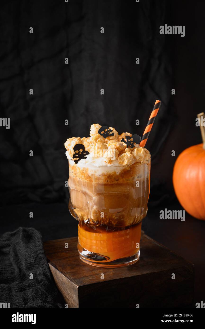 Halloween Kürbis Latte Kaffee mit Schlagsahne verzierten Totenköpfen und Popcorn in stilvoller Galss auf schwarzem Hintergrund. Stockfoto