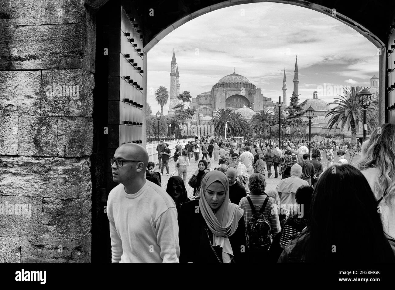 Touristen kommen durch eine Tür, die zur Blauen Moschee in der Nähe der Hagia Sophia in Istanbul, Türkei, in Schwarz und Weiß führt Stockfoto
