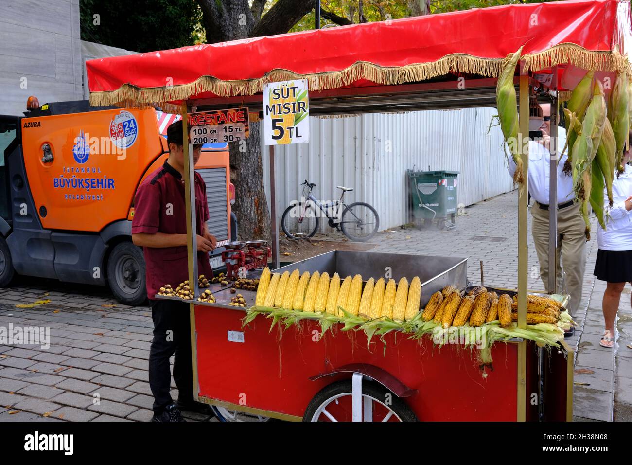 Mann, der gerösteten Mais auf dem Maiskolben und Kastanien in der Nähe des Sultanahmet-Platzes in Istanbul, Türkei, verkauft. Ein Tourist schnappte sich glücklich sein Bild Stockfoto