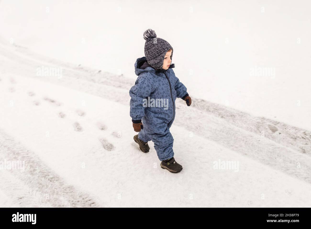 Kleiner Junge in blauem Einteiler, der selbstbewusst auf einem Schnee draußen läuft Stockfoto
