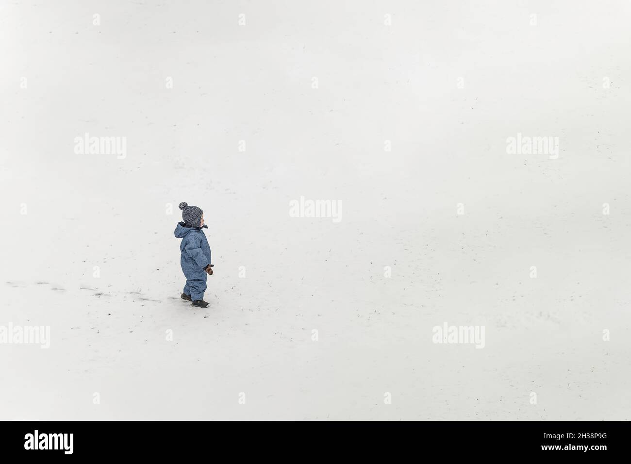 Kleiner Junge in blauer Winterkleidung Einteiler, der auf einem Schnee steht und l Stockfoto