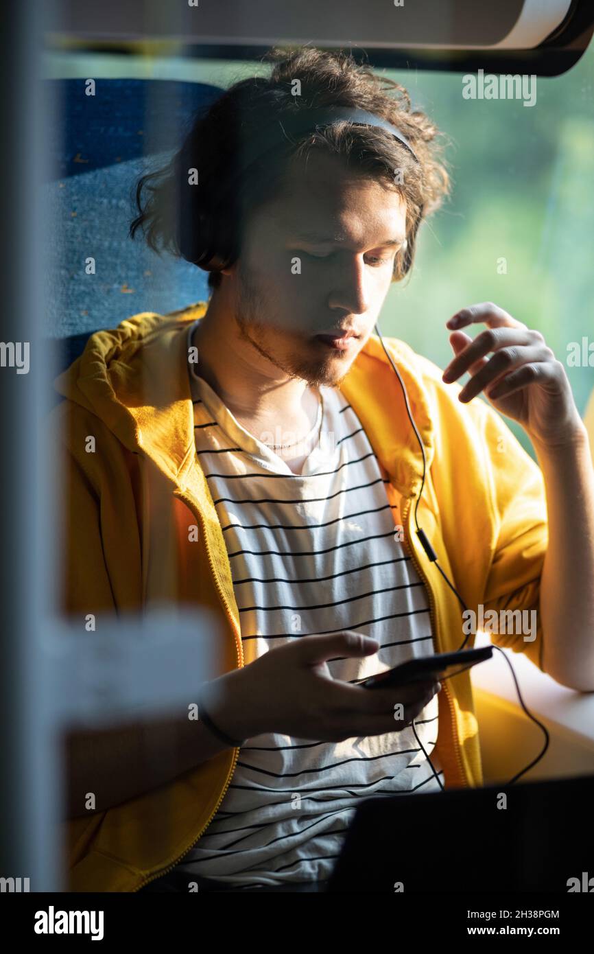 Junger Mann, Teenager mit Kopfhörern, im Zug unterwegs, Musik hören. Stockfoto