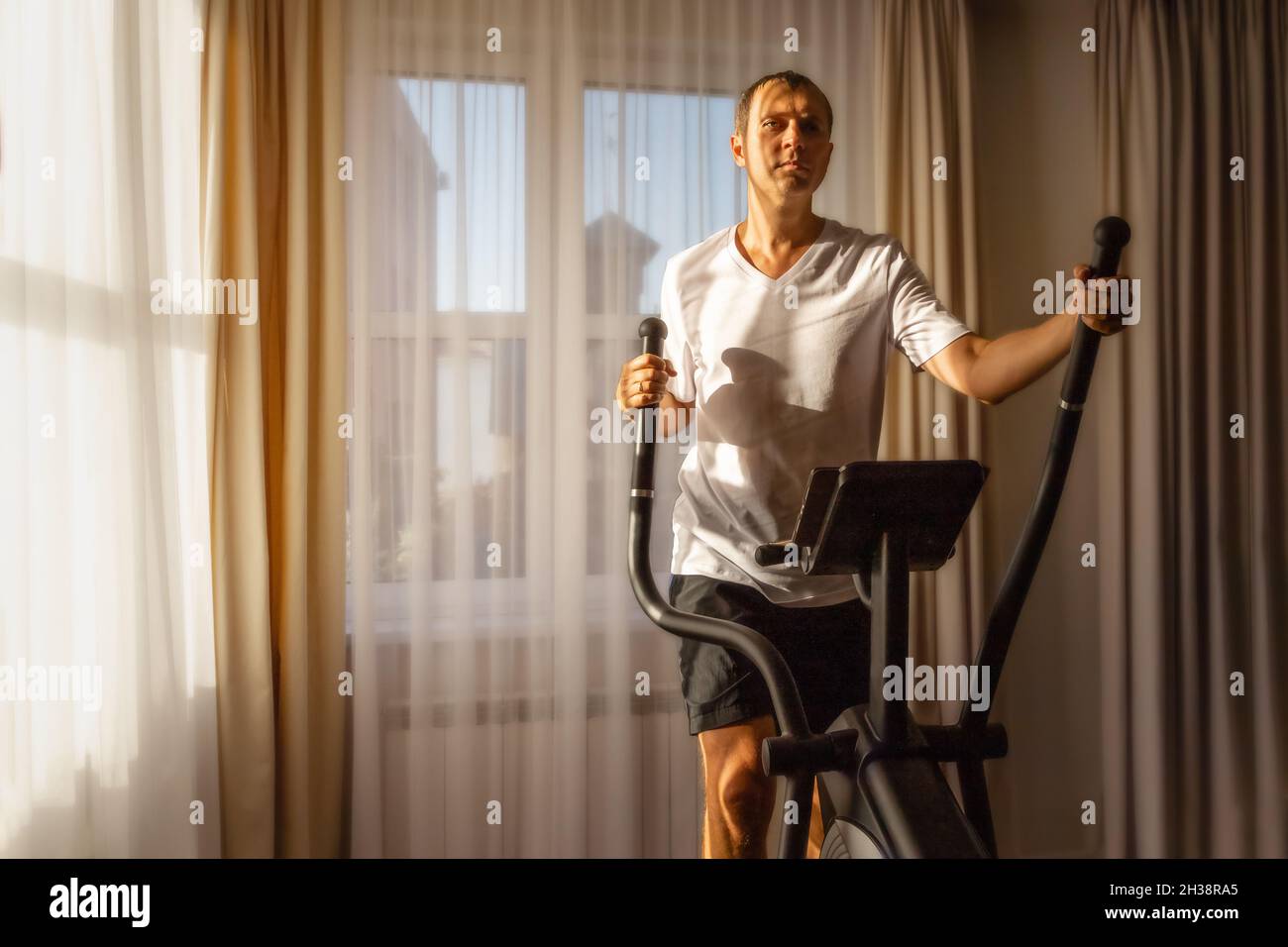 Ein Mann in einem weißen T-Shirt läuft zu Hause auf einem Ellipsoid Stockfoto
