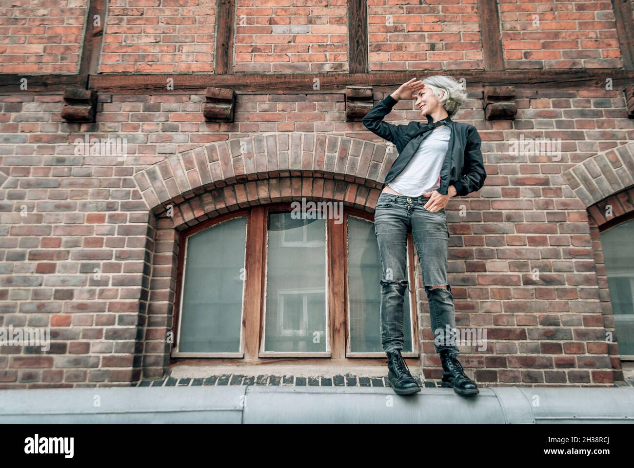 Frau steht auf einem Rohr in der Nähe des alten Gebäudes, lächelt und schaut weg Stockfoto
