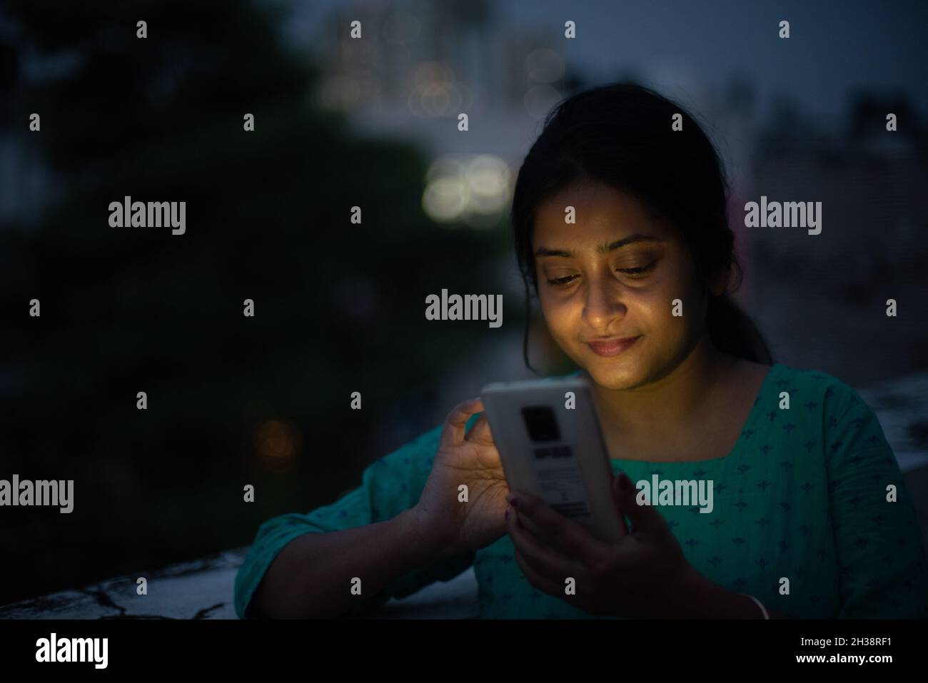 Junge Frau schaut in der blauen Stunde auf das Handy auf dem Dach Stockfoto