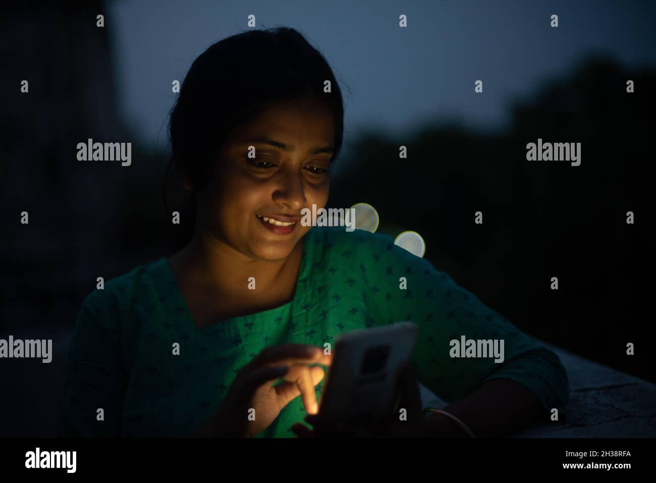 Junge Frau schaut in der blauen Stunde auf das Handy auf dem Dach Stockfoto