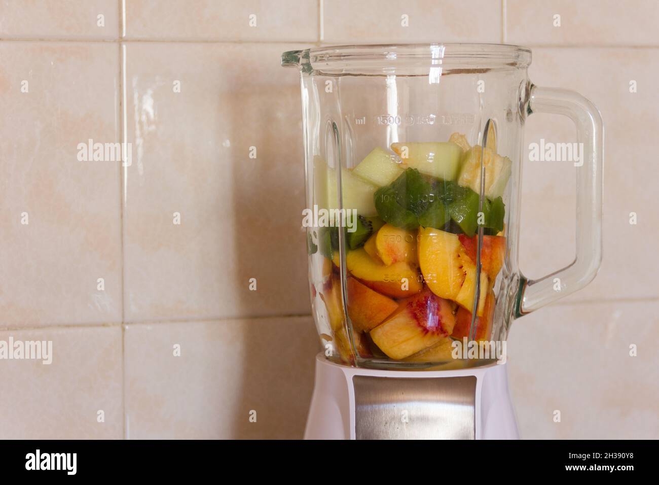 Fruchtmixer mit Pfirsich-, Kiwi- und Melonenstückchen. Glas, Lebensmittel, Getränke, gesunde Lebensmittel, Smoothie, Frühstück, Küche Elektrogeräte Konzepte Stockfoto