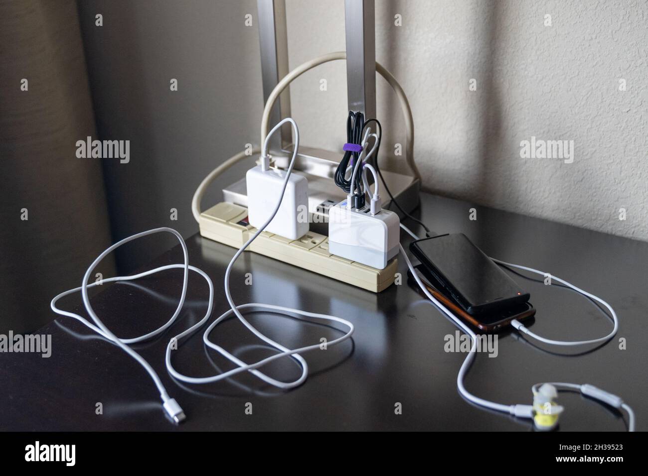 Unordnung von elektronischen Ladekabeln und Telefonen, die an eine Steckerleiste angeschlossen sind Stockfoto