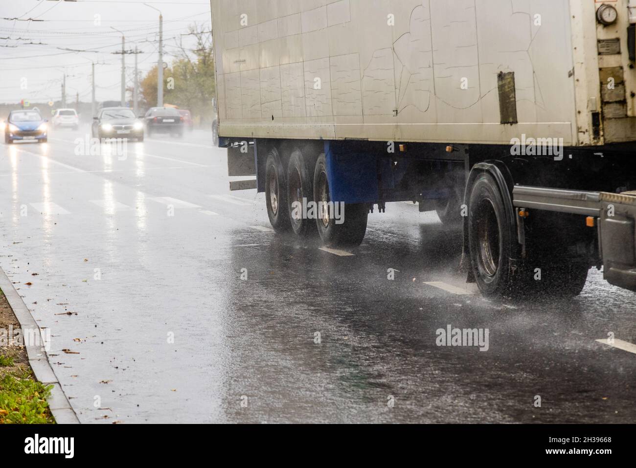 LKW mit trockenem Lieferwagen, der tagsüber auf einer nassen Straße mit Spritzern unterwegs ist Stockfoto
