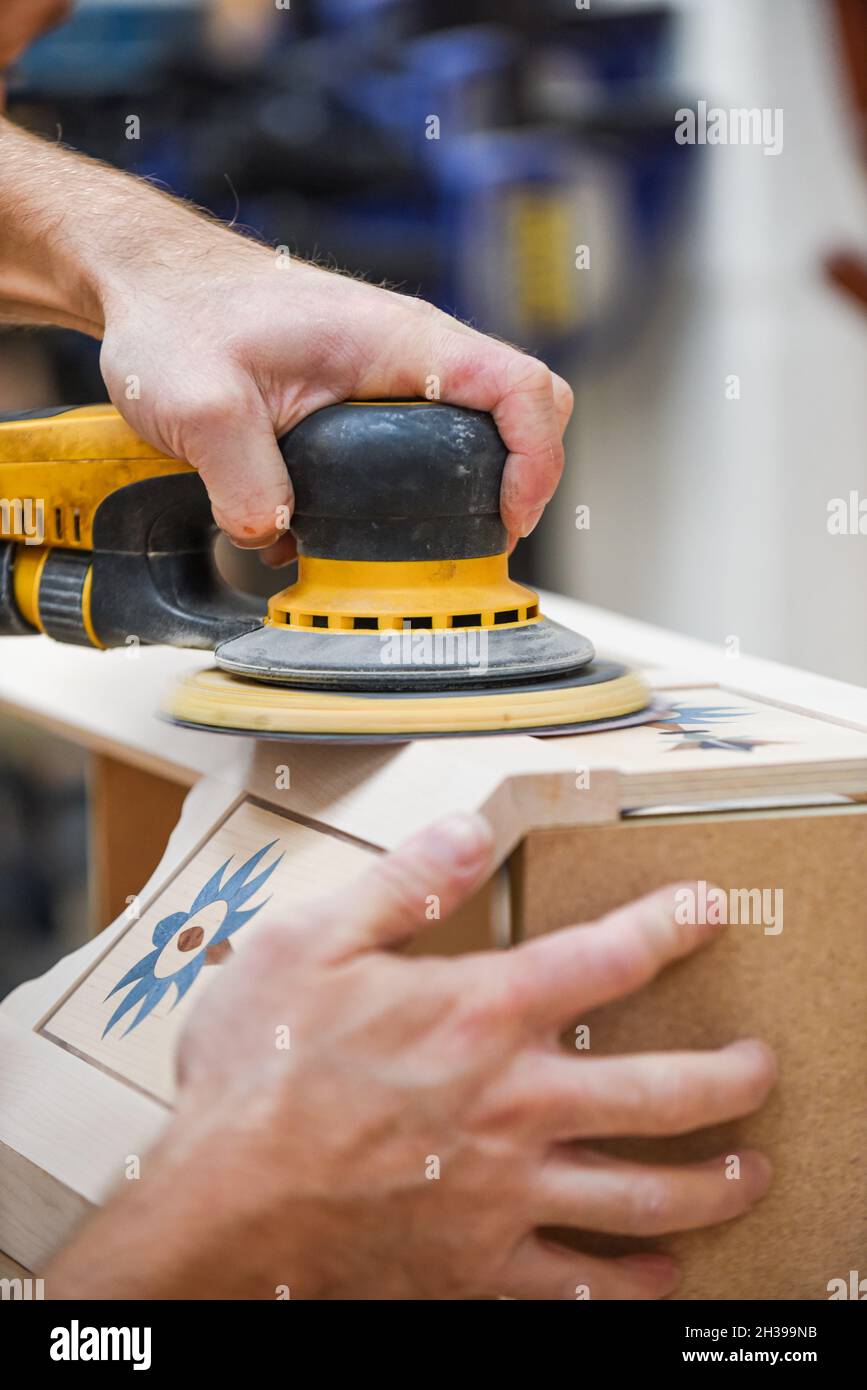 Ein Mann, der mit einem Elektroschleifer für Elektrowerkzeuge Holz in der Tischlerei basteln kann Stockfoto